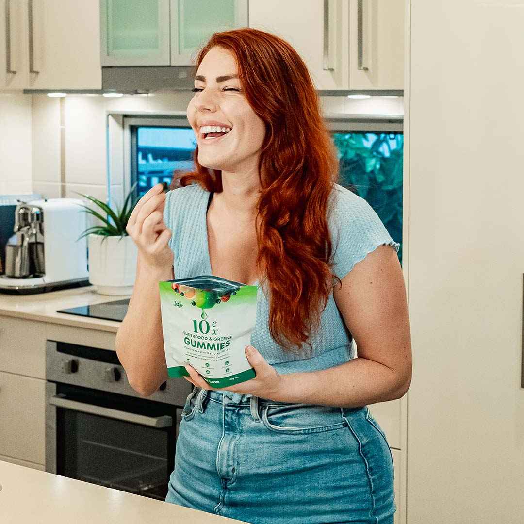 Smiling woman eating a Jaje Health Superfood Gummy in her kitchen.