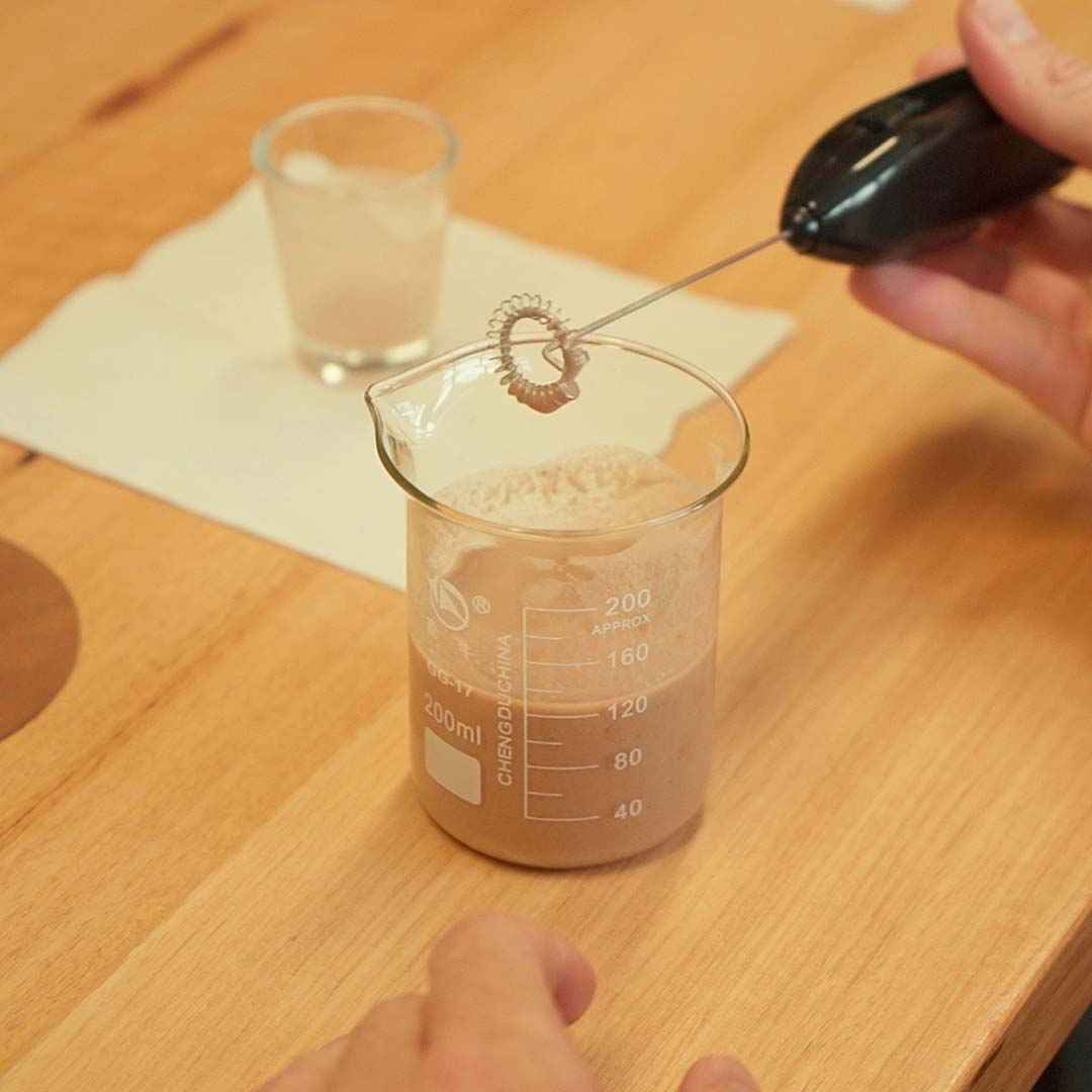 Hand using a frother to mix a Jaje protein shake in a 200ml beaker